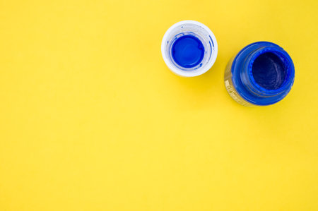A top view of a small opened can of blue gouache paint isolated on a yellow backgroundの写真素材