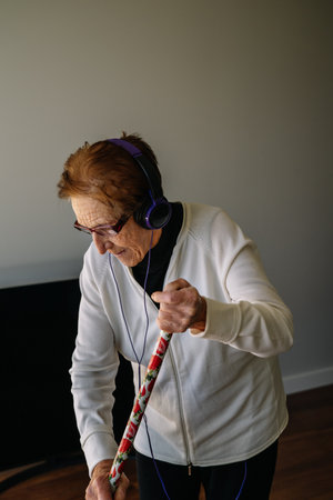 A senior female with headphones listening to music while sweeping the house