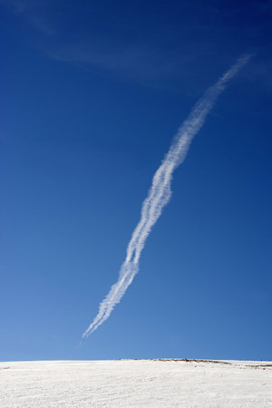 A vertical shot of vapor trail of an airplane in the blue skyの写真素材