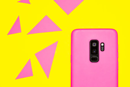 A top view of a pink smartphone on a yellow surface with colorful triangles on itの写真素材