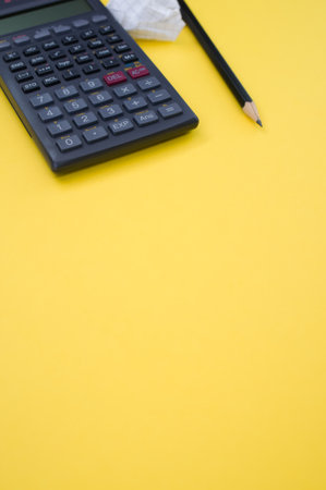 A vertical shot of a scientific calculator, pencil, grid notepad and a crumpled paper isolated on a yellow background with space for your textの写真素材