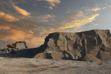 A large excavator working on an industrial site under a sunset skyの写真素材
