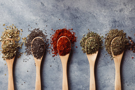 A top view of assortment of spices on wooden spoons: chia, paprika, parsley, rosemary, and teaの写真素材