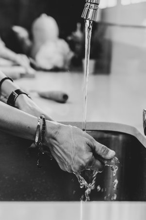 A grayscale shot of a female washing carrot in the kitchen sinkの写真素材