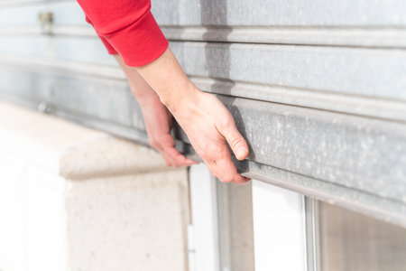 A man's hand closing metal roller shutter door