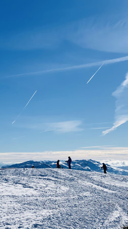 A vertical shot of the silhouette of the climbers on top of a snowy mountain on a sunny dayの写真素材