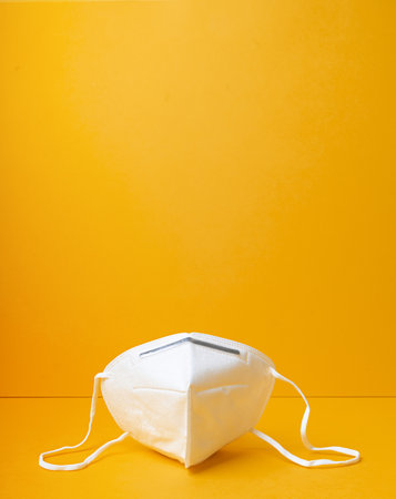 A closeup of a respiratory or surgical face mask on a yellow background. virus protection, pandemic or epidemic concept.の写真素材