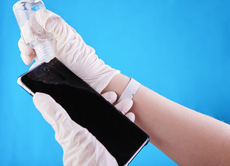 A woman's hand wearing white gloves cleaning the screen of a phone for protection against virus