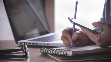 A female working from home using a laptop and taking notes in a notebook