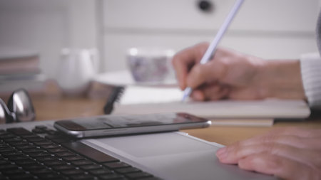 A female working from home using a laptop and taking notes in a notebook
