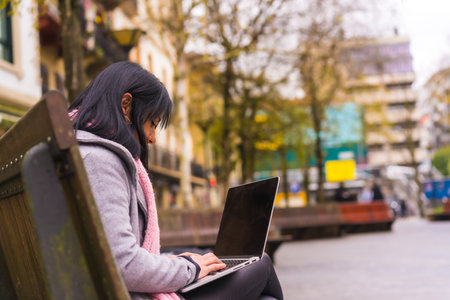 A beautiful caucasian female sitting on a bench and working with a laptopの写真素材
