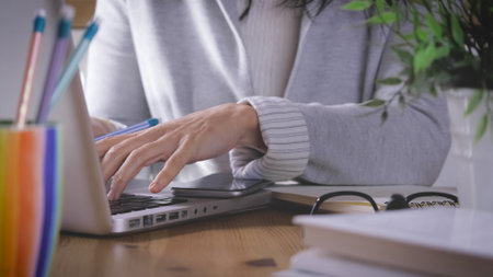 A female working from home using a smartphone, laptop and taking notes in a notebookの写真素材