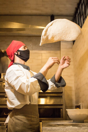 A vertical shot of dough flying through the air to become a disc in the chef's experienced hands