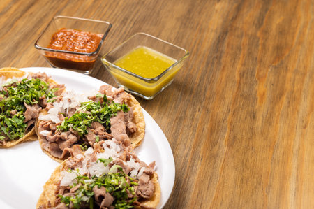 A closeup shot of delicious tortillas with beef, onions, and greens, and sauces on a wooden tableの写真素材