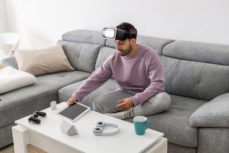 An adult man using a VR headset and a tablet while sitting on a sofaの写真素材