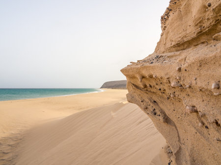 A beautiful shot of a rocky seacoast with soft sand and blue sea under the clear sky in Fuerte Ventura, Canary Islandsの写真素材