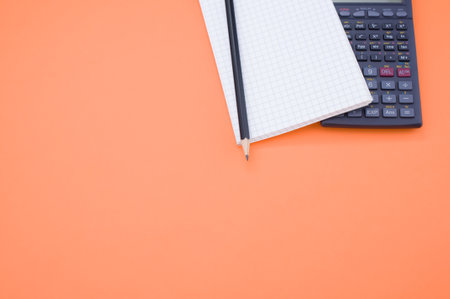 A partial view of a scientific calculator, notepad and pencil on orange background with space for...