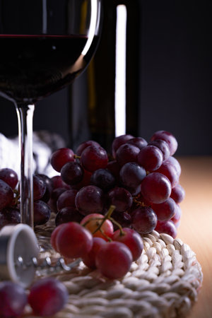 A vertical shot of a glass of red wine and grapes on a tableの写真素材