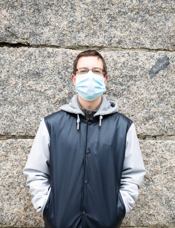 A vertical shot of a European tourist in glasses and facial mask standing near a wall - new normal conceptの写真素材
