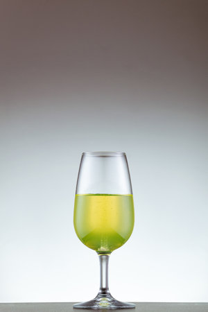 A vertical shot of a small Champagne glass with green alcohol isolated on a gray backgroundの写真素材