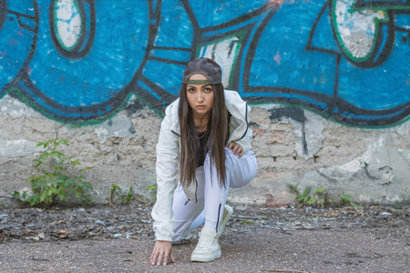 A young girl in a white tracksuit sits in a low start and prepares for a run on a concrete trackの写真素材