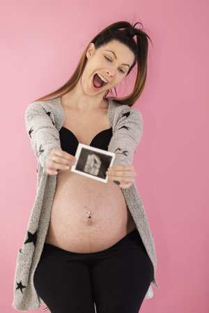Excited looking pregnant woman holding an out of focus printed obstetrician ultrasound scan in front of her. Selective focus. Pregnancy concept.の写真素材