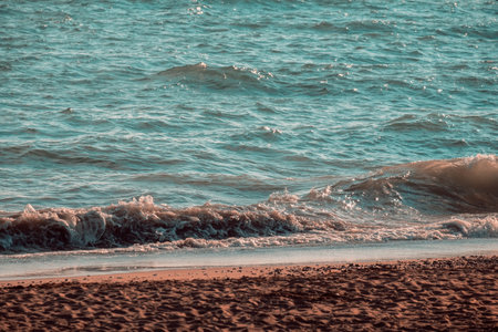 A closeup shot of afoam waves hitting a sandy seashoreの写真素材