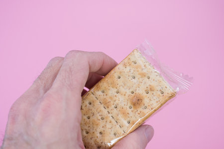 A closeup shot of a person holding crackers in a plastic bag isolated on a pink backgroundの写真素材