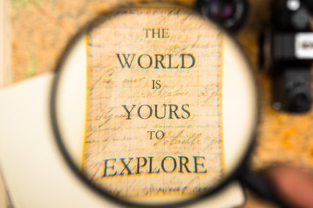 A vintage history paper with the writing ''The World is Yours to Explore'' seen through a magnifying...