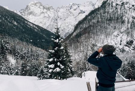 A closeup shot of a guy taking pictures of snow-covered hills and mountainsの写真素材
