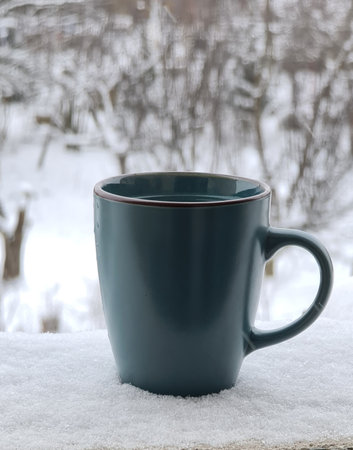 A vertical shot of hot tea in a mug with a winter landscape in the backgroundの写真素材