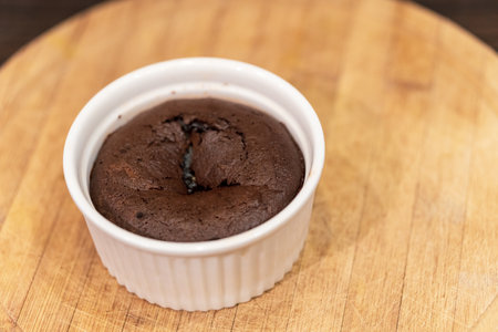 A  tastychocolate muffin in a small white cup on a wooden surface