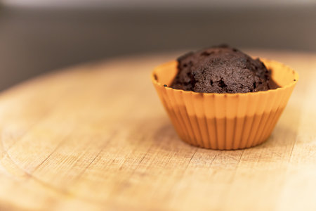 A closeup shot of a chocolate muffin in an orange paper placed on a wooden surfaceの写真素材