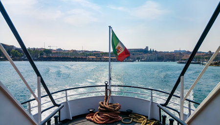 Italian flag on white pole on stern of ship. Lake, sea, summer, sunny day. Lago di Garda, Lake Garda, Desenzano, Italy.の写真素材