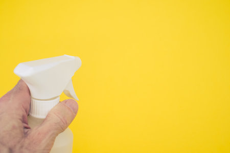 A man's hand holding a white plastic spray bottle against a yellow backgroundの写真素材