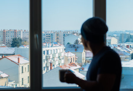 A young man drinking coffee and looking out the window at the snowy cityの写真素材