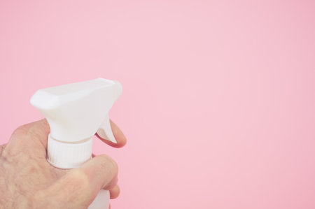 A man's hand holding a white plastic spray bottle against a pink backgroundの写真素材
