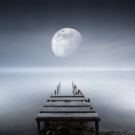 An old broken pier in the sea and the moon on the horizonの写真素材