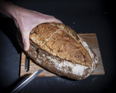 A man's hand with freshly baked bread on a wooden cutting board with a knife