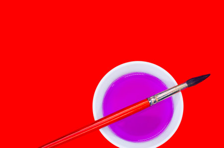 A closeup shot of a brush with a pink paint bowl on a red backgroundの写真素材