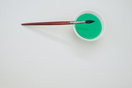 A closeup shot of a brush with a green paint bowl on a gray backgroundの写真素材