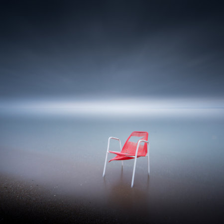 A broken red chair on the sand at the beachの写真素材