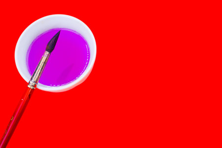 A closeup shot of a brush with a pink paint bowl on a red backgroundの写真素材