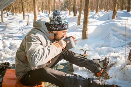 Bushcrafter drinks hot tea while sitting in a camp during winter frost