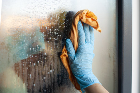 A closeup shot of a hand in glove cleaning window with yellow clothの写真素材