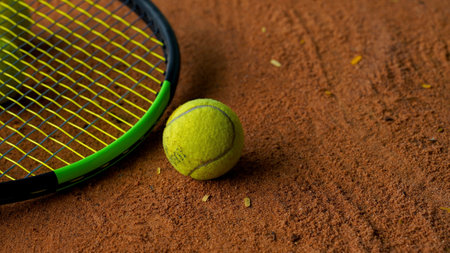 A closeup of the yellow tennis ball with a racket in the clay courtの写真素材