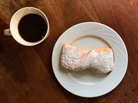 A top view of baked good with powdered sugar and black coffee in a mug on the wooden tableの写真素材