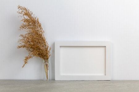 A dried grass in a clear glass beside a white frameの写真素材