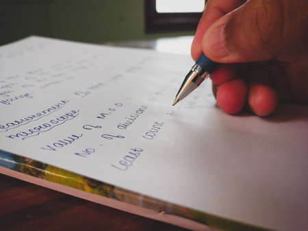 A closeup shot of a hand of a person with pen writing a text on the white paper