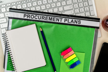 A notepad with a pencil on a green folder labelled "PROCUREMENT PLANS" on a laptop in the officeの写真素材